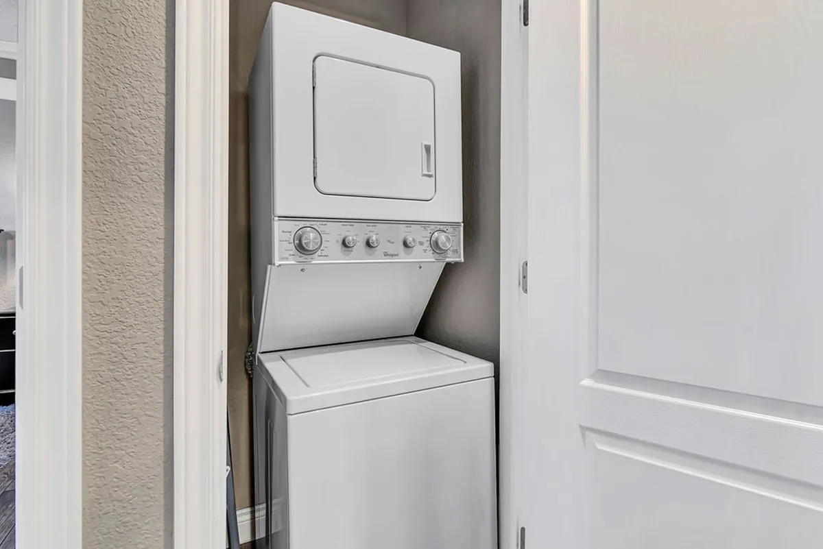A bright and practical interior space featuring a stacked washer and dryer unit, white cabinetry, and a neutral color palette. The area is clean and organized, emphasizing convenience for guests managing laundry during their stay.
