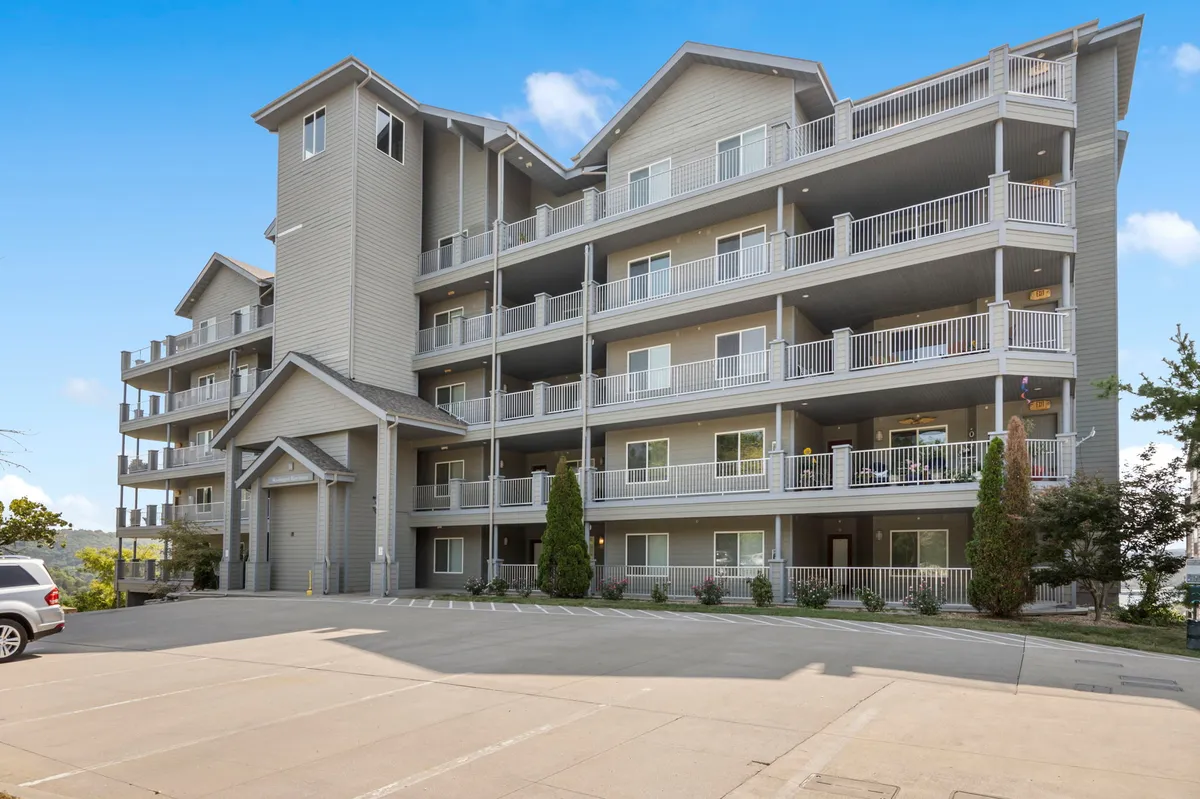This image captures the entrance to a four-story condominium building with several balconies and a spacious entryway. The area is inviting, with open views for guests to enjoy morning coffee or socialize outdoors. The scene embodies the welcoming and accessible atmosphere ideal for mature and multi-generational groups.