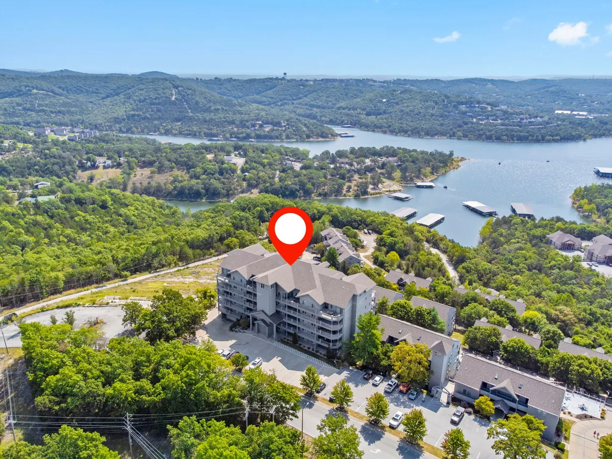A tranquil exterior scene showing the lake surrounded by gentle hills, with the property building and boats in view. The natural walking trails leading toward the lake are implied, and the overall setting is peaceful and scenic, inviting outdoor exploration and relaxation.