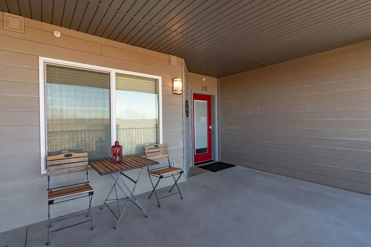 A small, intimate outdoor seating area with a table, two chairs, and a lantern sits just outside a red door. The setup is shaded and peaceful, ideal for enjoying a quiet coffee or conversation while soaking up views and fresh air.