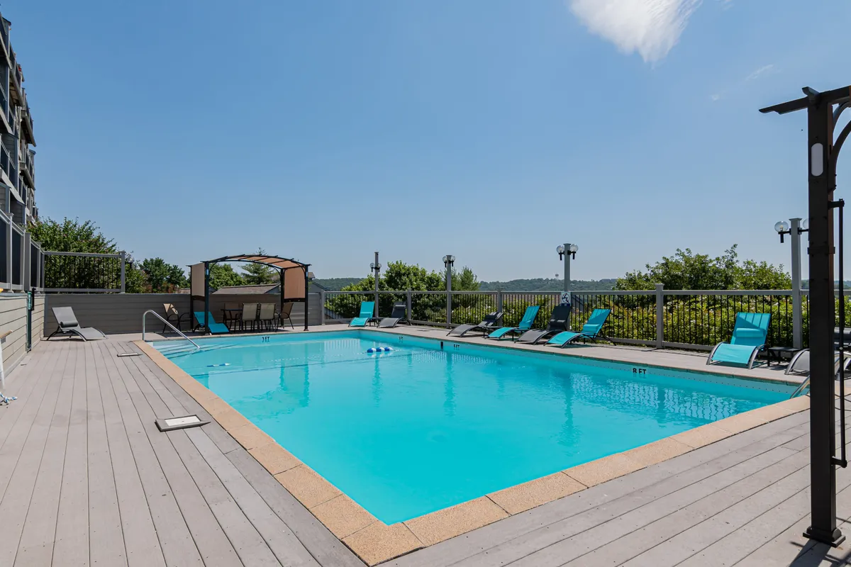This image showcases the inviting outdoor swimming pool surrounded by lounge chairs and a canopy structure, with a landscaped view beyond. The pool environment looks leisurely, ideal for relaxation, sunbathing, and social gatherings. The area radiates a resort-like atmosphere.