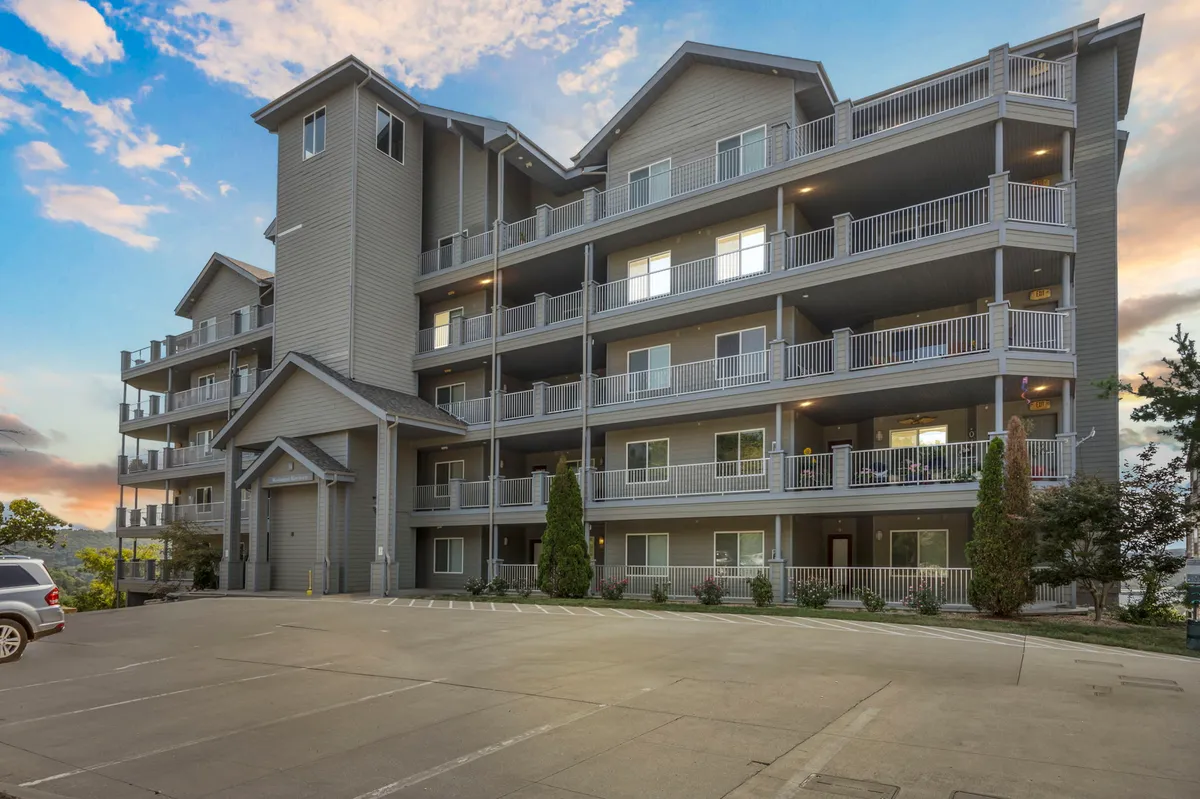 The image showcases the exterior of a multilevel condominium building surrounded by well-maintained landscaping. Several balconies overlook the green communal spaces, inviting guests to relax outdoors and enjoy the sunset. The overall setting feels peaceful and welcoming, reflecting the tranquility described in the section content.