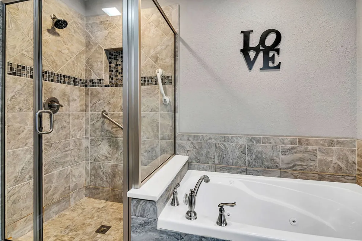 A luxurious bathroom featuring a glass-enclosed shower, a spacious jetted jacuzzi tub, and a decorative 'LOVE' sign that adds a personal touch. The space feels spa-like and indulgent—perfect for unwinding after a long day.