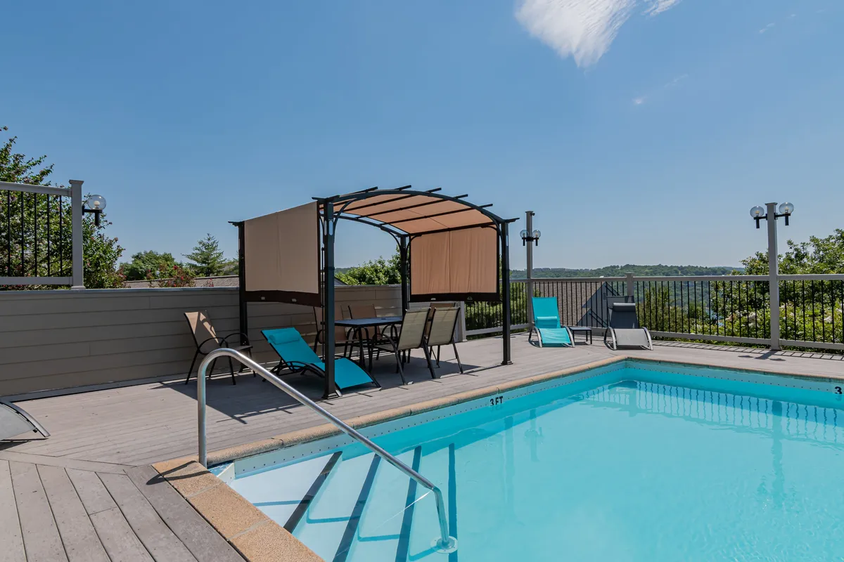 This image features a spacious outdoor swimming pool surrounded by a canopy seating area and lounge chairs, set against a backdrop of greenery. The pool area is inviting for both relaxation and social gatherings, with plenty of seating for groups of friends or couples to unwind together. Soft lighting and open sky suggest a perfect place for both daytime fun and evening lounging.
