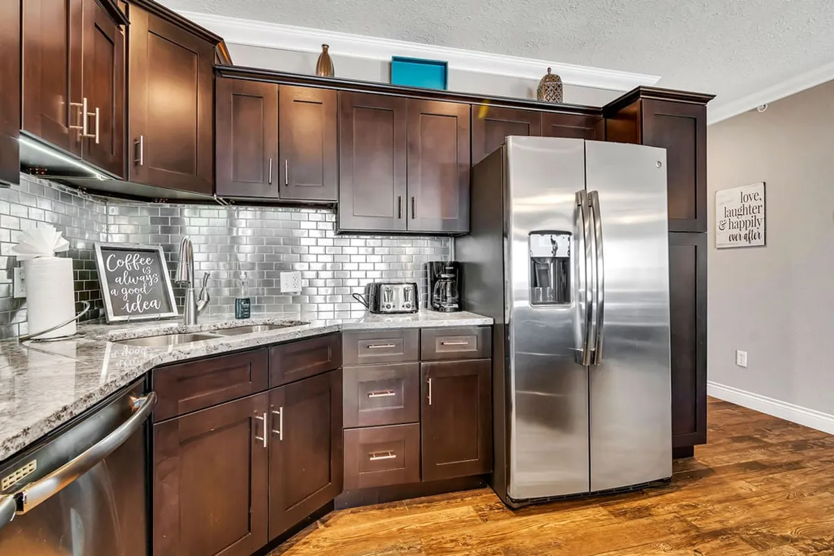 This kitchen scene features a stainless steel refrigerator, granite countertops, dark wood cabinetry, and tasteful decorative wall art. The setting appears ready for socializing and entertaining while cooking, adding a personal, inviting touch.