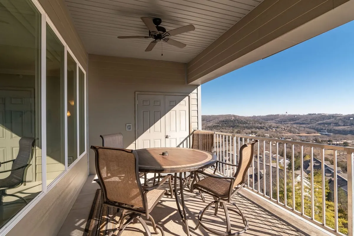 A private exterior deck featuring a round table and four chairs, set against a backdrop of panoramic mountain and lake views. Sliding glass doors indicate seamless indoor-outdoor access, ideal for morning coffee or evening toasts while immersed in nature.