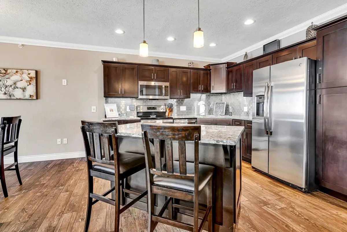 The image showcases a beautifully remodeled kitchen with a prominent kitchen island, dark cabinetry, and gleaming stainless steel appliances under warm pendant lighting. The granite countertops stand out, and the space feels open and inviting, perfectly capturing the heart of the kitchen area.